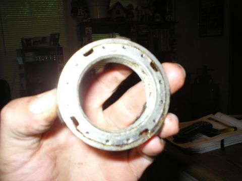 1986 Ford Bronco - A metal bearing or seal is held up for inspection, showing its circular shape and small holes.