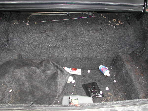 Car trunk interior with a spare tire covered by a black cloth, a blue and white bottle, and debris