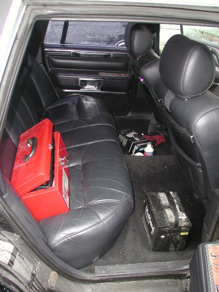 1987 Lincoln Town Car - Interior view of a car's back seat area with a toolbox and car battery present.