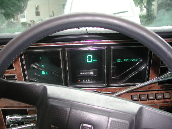 Green digital dash cluster reading 0 MPH with OIL PRESSURE display and woodgrain trim