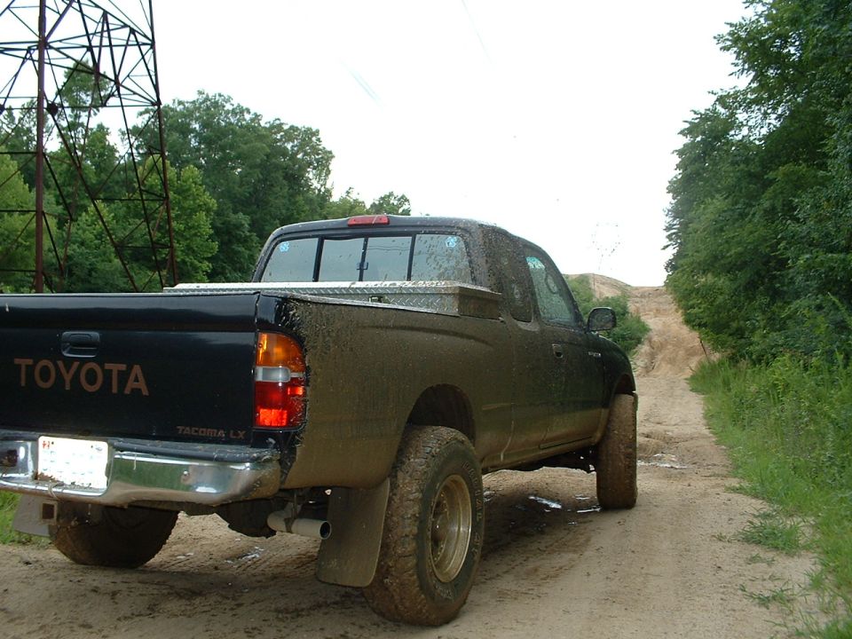 Muddy Toyota Tacoma pickup truck on a dirt road going uphill