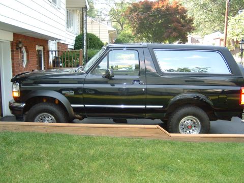 1993 Ford Bronco - A black 1993 Ford Bronco is parked on a wooden platform next to a house.