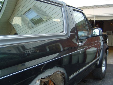 1993 Ford Bronco - Side profile of a black 1993 Ford Bronco, showing some body damage near the rear wheel well.