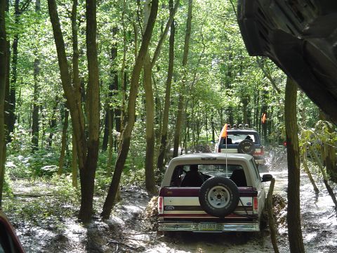 1993 Ford Bronco - Multiple off-road vehicles navigate a muddy, wooded trail.