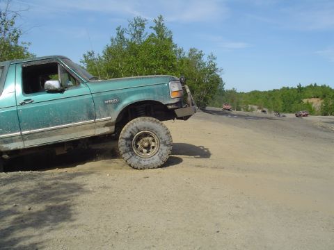 1993 Ford Bronco - A green 1993 Ford Bronco navigates a dusty off-road trail with other vehicles in the background.