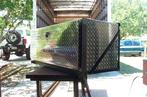 1995 Ford Bronco - A Delta Pro diamond-plate aluminum toolbox mounted in a black welded steel frame sits on a work table outdoors, with the open box body of a…