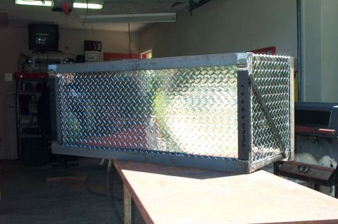 1995 Ford Bronco - A bare-steel welded mounting frame wrapped around a diamond-plate aluminum toolbox, resting on a wooden bench in a garage shop. Fresh weld…