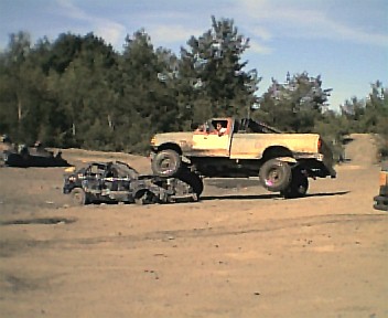 1985 Ford Bronco - Ford pickup truck crushing a car in a demolition derby or off-road event.