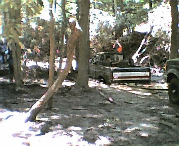 1985 Ford Bronco - A 1980s Ford Bronco is seen in a wooded area with other vehicles and debris.