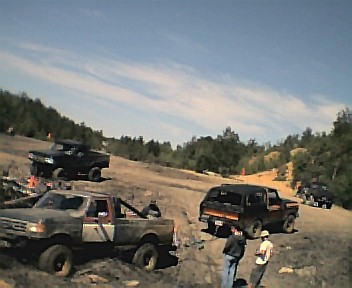 1985 Ford Bronco - Multiple off-road vehicles navigate a challenging dirt terrain on a sunny day.