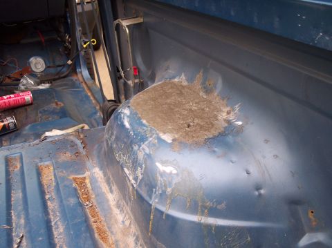 1990 Ford Bronco - The interior of a blue vehicle displays rust damage and a patch of body filler on the rear wheel well, indicating repair work.