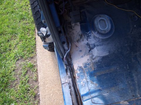 1990 Ford Bronco - The interior floor of a blue vehicle shows signs of rust and damage, with wiring exposed near the door.