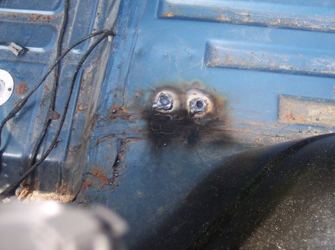 1990 Ford Bronco - Close-up of rusted blue metal floor with two welded nuts and wiring.
