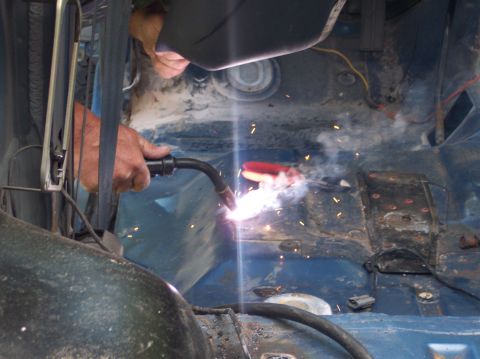 1990 Ford Bronco - A person welds the interior floor of a vehicle, with sparks flying.
