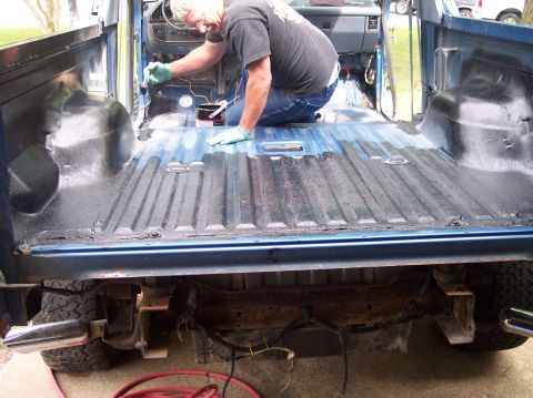 1990 Ford Bronco - Rear view into the stripped rear cargo area of a blue Ford Bronco with the tailgate, rear seats and interior trim removed, as a man in glov…