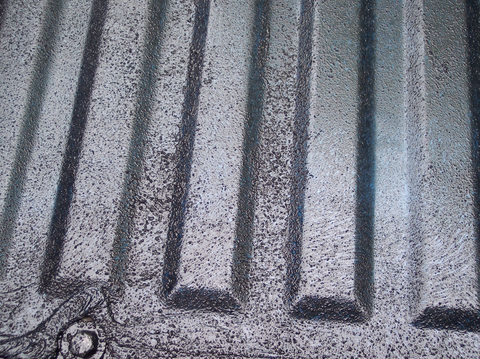 Close-up of ribbed floor pan sanded to bare metal with blue paint traces