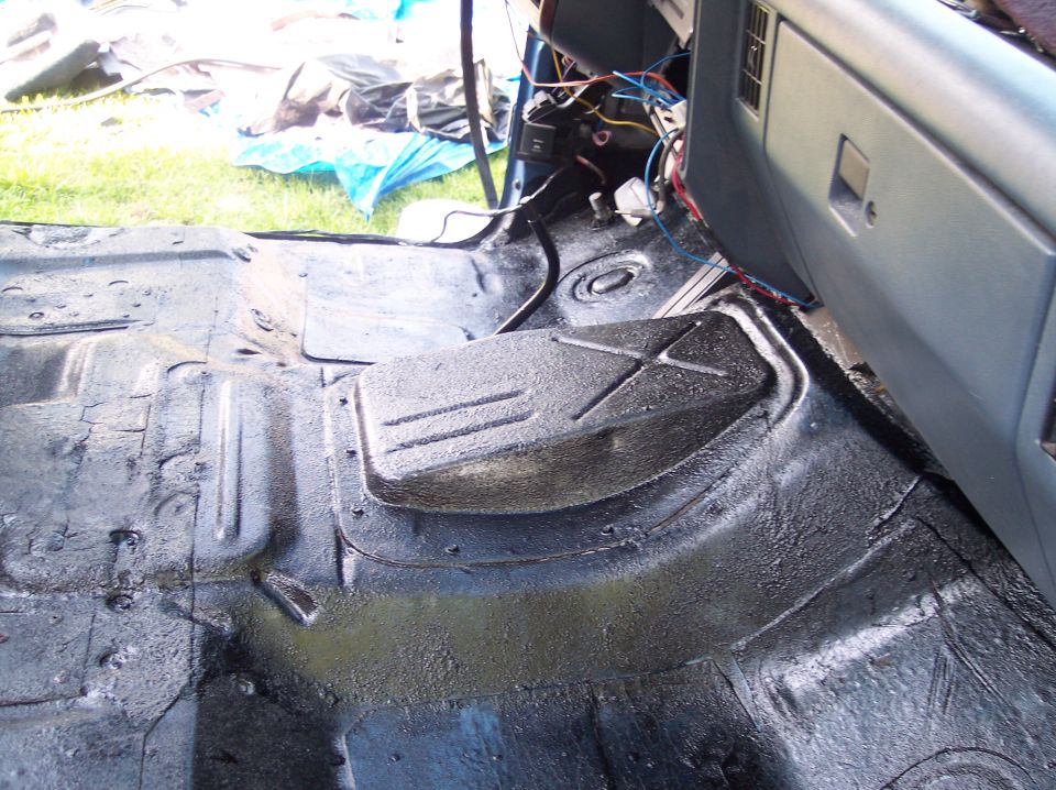 Gutted cab floor pan and trans tunnel coated in black bedliner, wiring hanging from dash