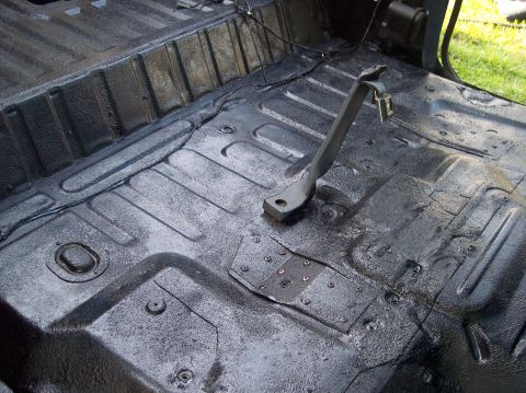 1990 Ford Bronco - The interior floor of a vehicle, coated in black texture paint, reveals exposed metal and wiring, along with a brake pedal assembly.