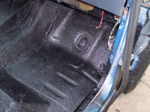 1990 Ford Bronco - Close view of a bare cab floor pan freshly rolled in wet, glossy black bedliner, showing the stamped body plug and seat mount depressions.…
