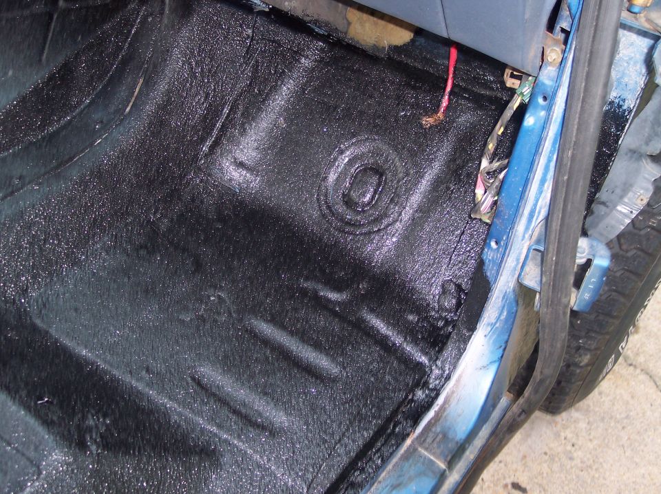 Wet black bedliner coating on bare floor pan beside blue door sill