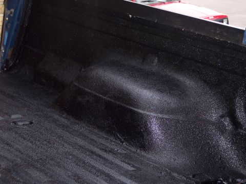 1990 Ford Bronco - The textured surface of a freshly applied truck bedliner is shown, with a red vehicle in the distance.