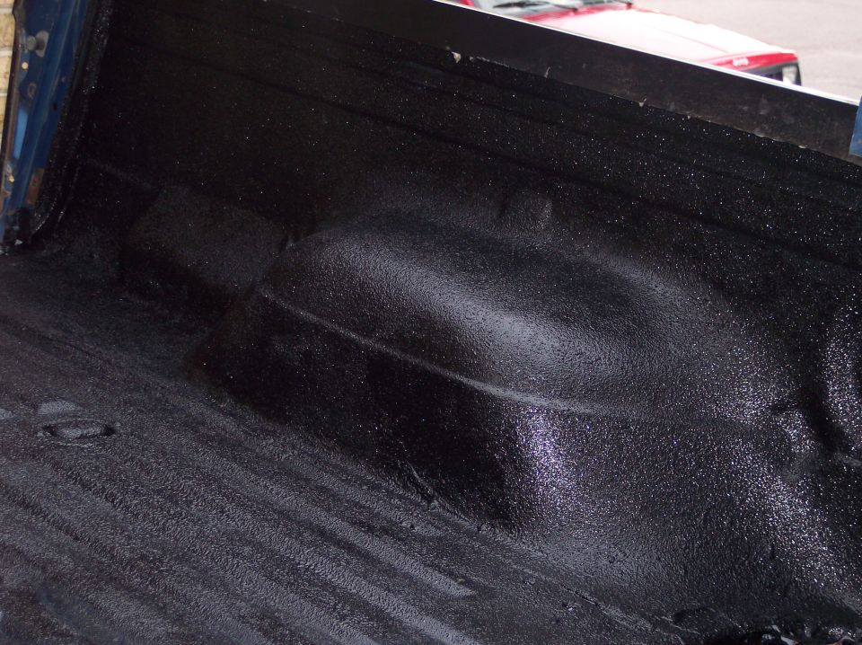 Close-up of a black spray-in bedliner in a truck bed. Another vehicle is visible in the background