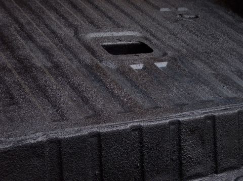 1990 Ford Bronco - Close-up of a dark, textured truck bedliner showing its ribbed surface and a central rectangular opening.