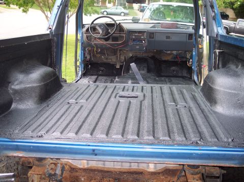 1990 Ford Bronco - View forward through the open tailgate opening of a blue Ford Bronco stripped to bare metal inside, with the entire rear floor, wheel tubs…
