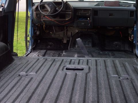 1990 Ford Bronco - Low interior shot across the ribbed rear floor of a Ford Bronco freshly coated in textured black bedliner, looking forward to the gray dash…