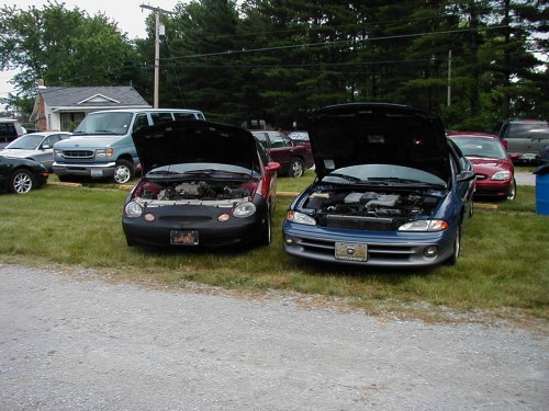 Two sedans with hoods open parked on grass at a car meet