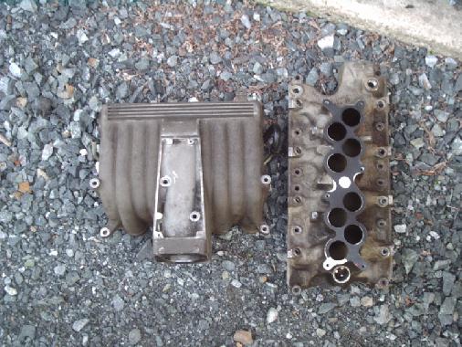 Upper and lower V8 aluminum intake manifold halves lying on gravel driveway