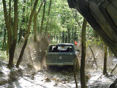 1993 Ford Bronco - A Ford Bronco navigates a muddy path in a forest, with another vehicle partially visible in the foreground.