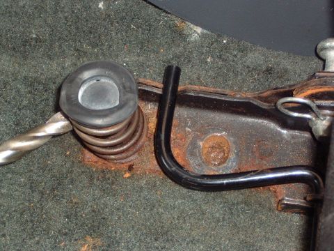 1993 Ford Bronco - A close-up view of a rusty seat spring mechanism with a rubber grommet and a metal rod, showing some wear and wear.