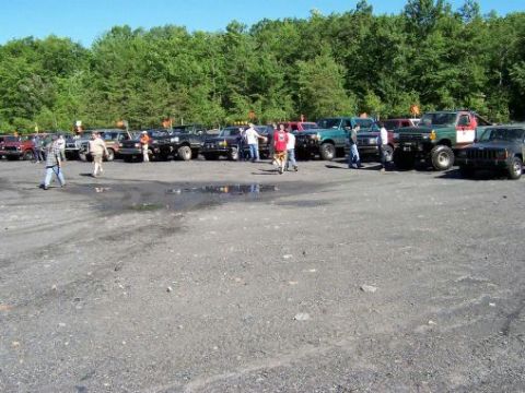 1996 Ford Bronco - Several off-road vehicles are parked in a lot, with a group of people gathered around them.