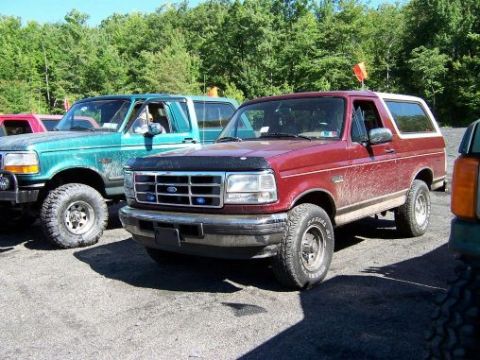 1996 Ford Bronco - Two Ford Broncos are parked side-by-side on a gravel lot with trees in the background.