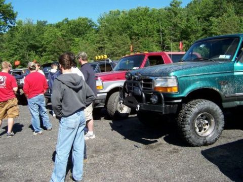 1996 Ford Bronco - Several people gather around a green Ford Bronco and other trucks at an outdoor event.