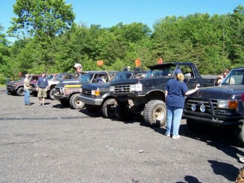 1996 Ford Bronco - Several lifted Ford trucks and SUVs are parked in a line, with a black Bronco prominently featured in the foreground.