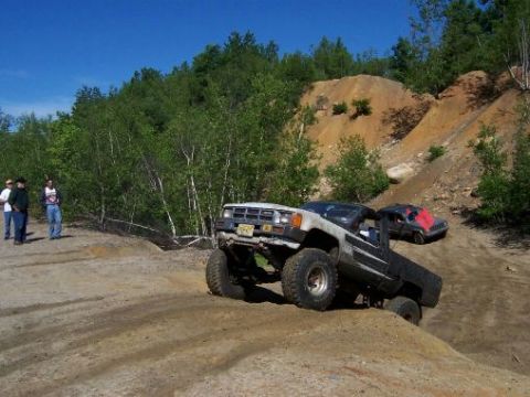 1996 Ford Bronco - Two off-road vehicles navigate a challenging dirt terrain under a clear blue sky.