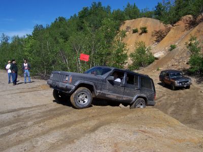 1996 Ford Bronco - Two Jeep Cherokees navigate a challenging off-road course on a sunny day.