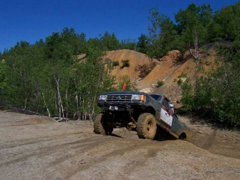 1996 Ford Bronco - Off-road pickup truck navigating a challenging dirt terrain under a clear blue sky.