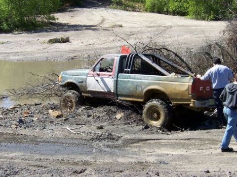 1996 Ford Bronco - A modified Ford pickup truck is stuck in a muddy, watery area with two people observing.