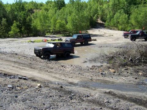 1996 Ford Bronco - Several off-road vehicles navigate a muddy terrain under a clear sky.