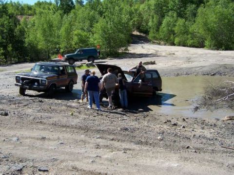 1996 Ford Bronco - Several off-road vehicles are in a muddy area with people attending to one that appears to be stuck.