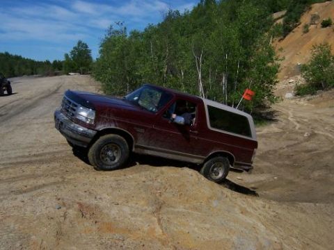 1996 Ford Bronco - This Ford Bronco navigates a challenging off-road course under a bright blue sky.
