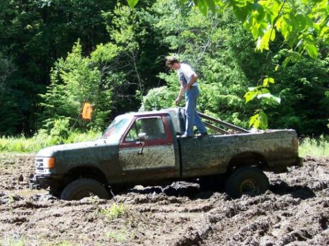 1996 Ford Bronco - A man stands in the bed of a mud-covered Ford F-Series truck as it is stuck in a muddy field.