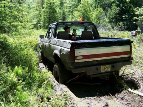 1996 Ford Bronco - A 1996 Ford Bronco navigates a muddy trail, with a second vehicle partially visible in the distance.
