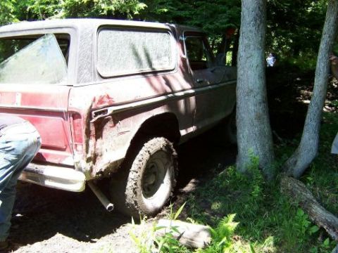 1996 Ford Bronco - A red SUV is stuck in the mud, with its rear window broken and body dented.