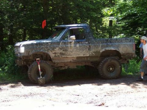 1996 Ford Bronco - A heavily muddied pickup truck sits off-road with a shovel nearby, suggesting recent off-road activity.