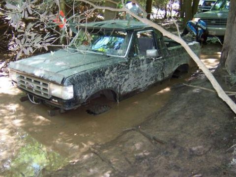 1996 Ford Bronco - Mud-covered 1992 Ford F-150 pickup truck stuck in muddy water with another vehicle in the background.
