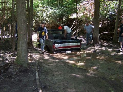 1996 Ford Bronco - A group of people are gathered around a truck that is stuck in a muddy, wooded area.